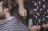 Barber's hands holding scissors while shaping a classic pompadour hairstyle.