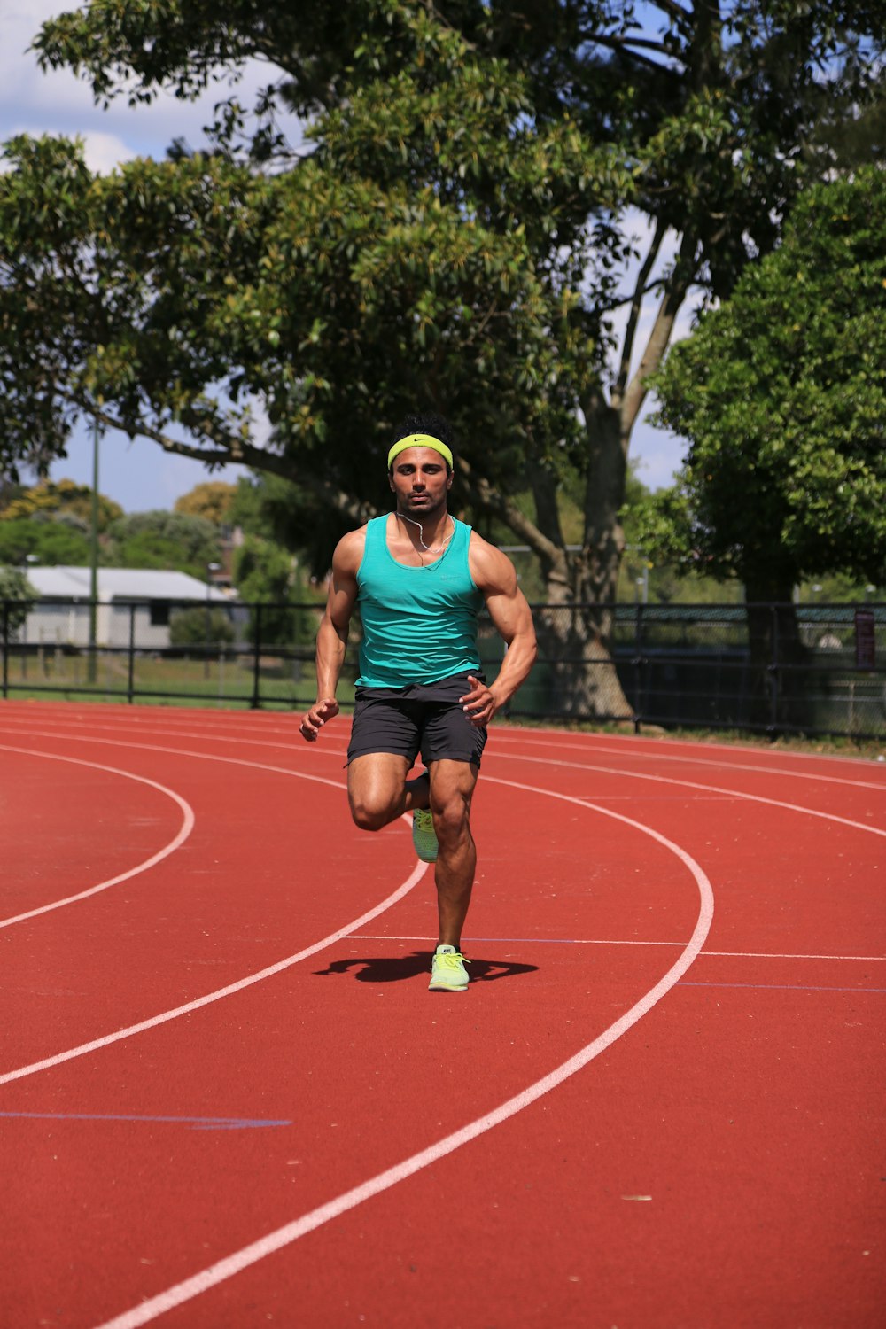 man in green tank top running on track field during daytime