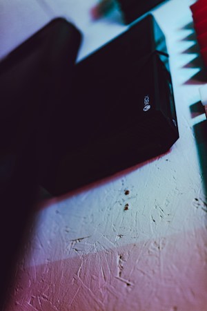 A close-up of a textured wall with a gaming console placed at an angle. The lighting creates a dramatic contrast with shades of blue, red, and pink highlighting the surface.