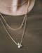 person wearing silver necklace with silver pendant