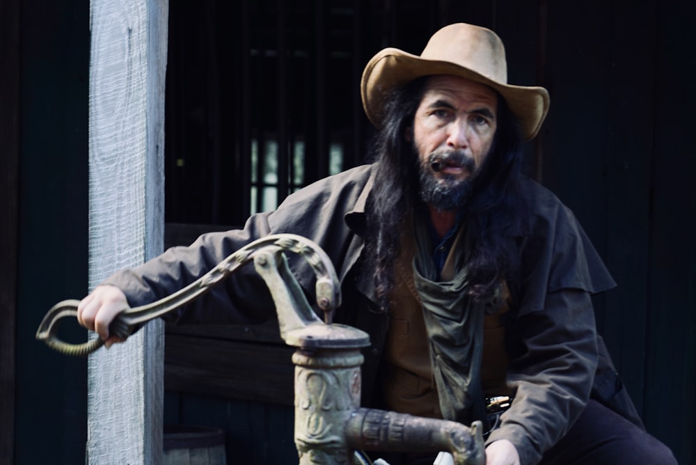 man in brown cowboy hat and black leather jacket sitting on black metal fence during daytime