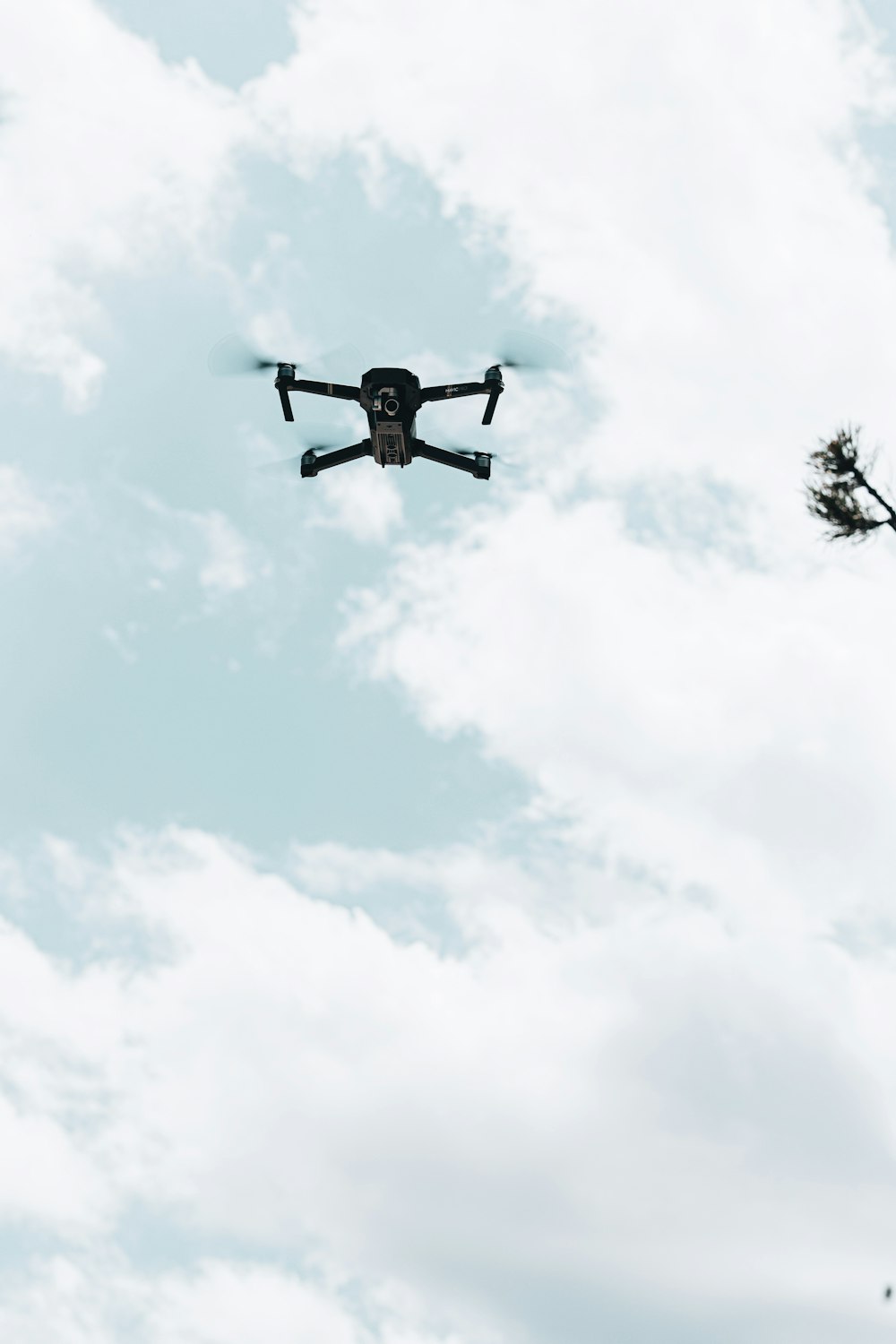 black and white drone flying under white clouds during daytime