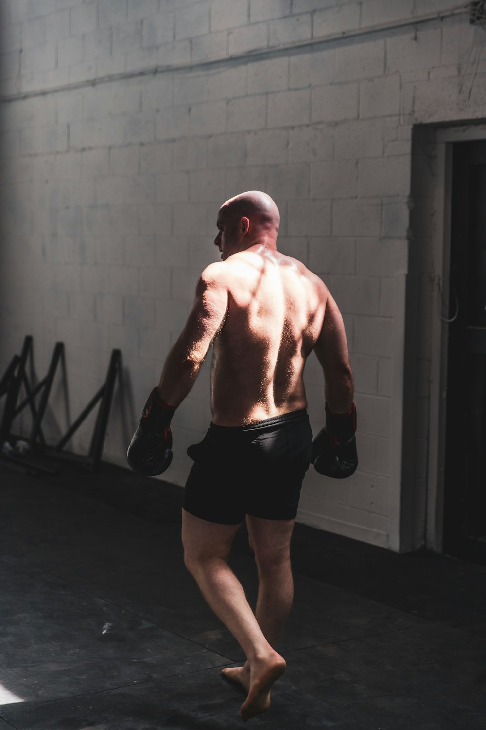 topless man in black shorts standing near gray wall