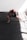 A bald individual is training with boxing gloves in a well-lit room, crouched low in a dynamic stance with one leg extended. The floor is covered with dark mats, and sunlight streams in through large windows, casting bright patterns across the room.