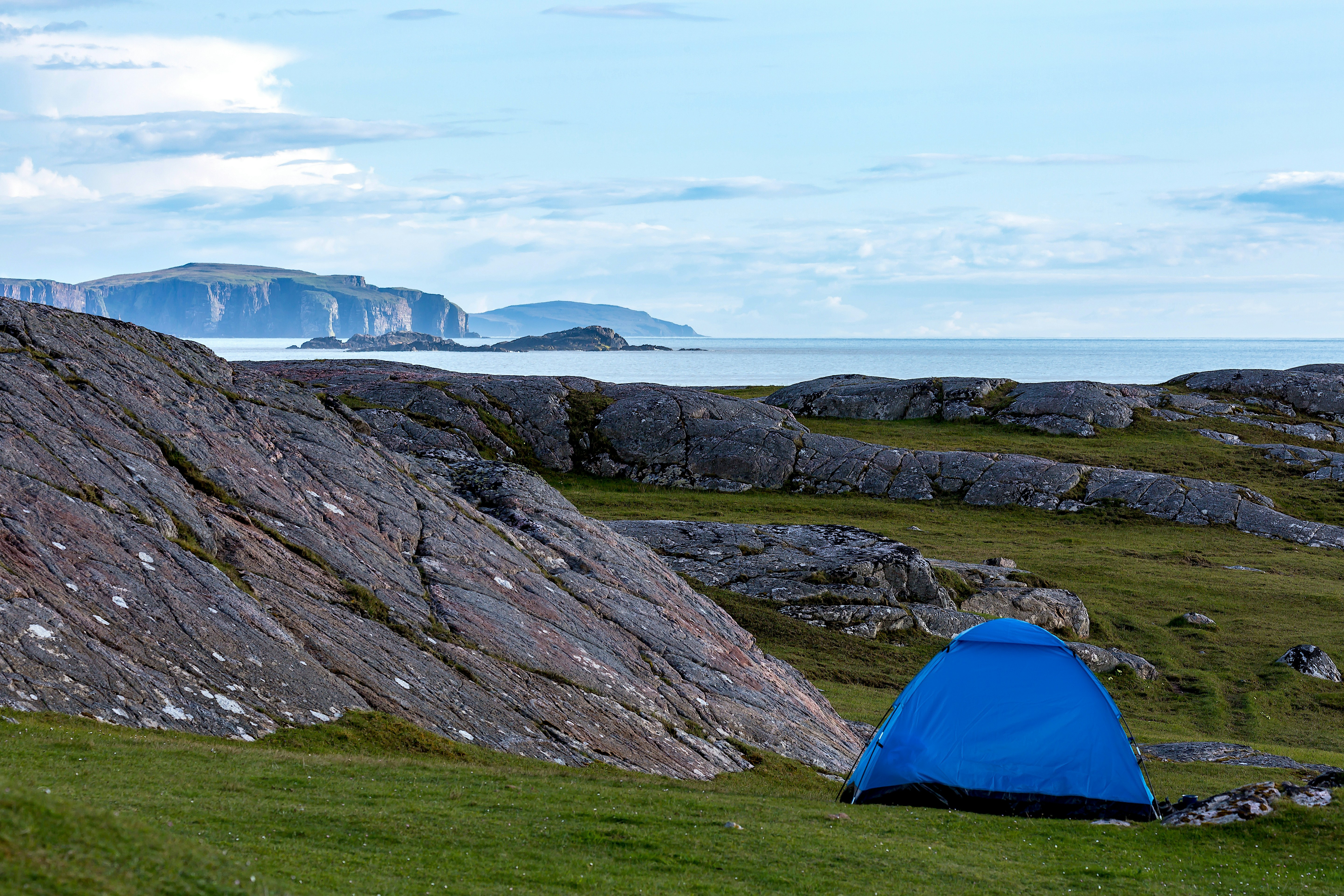 blue dome tent on green grass field near mountain under white clouds during daytime leisure activity teams background