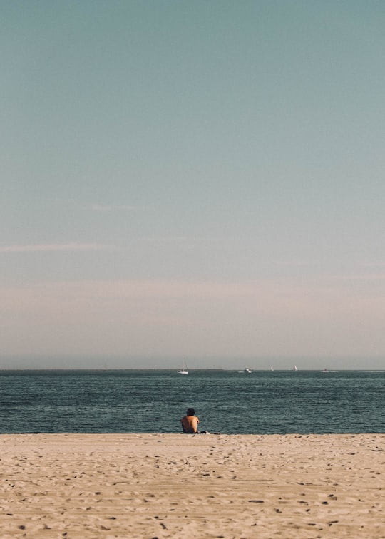 person in black shirt sitting on brown sand near body of water during daytime in Long Beach United States