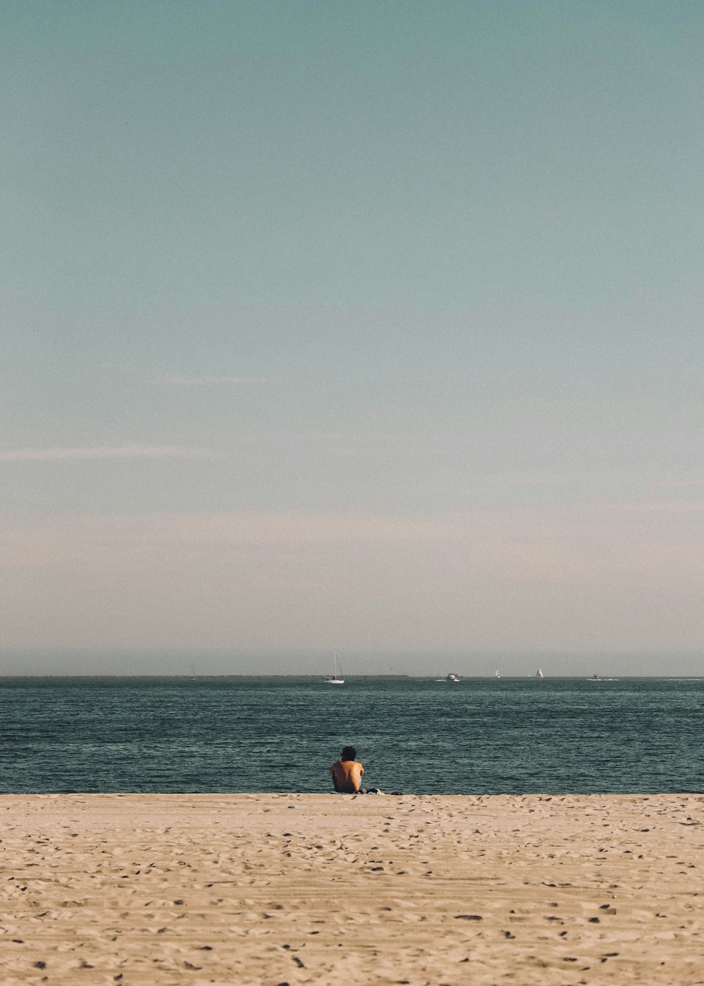 person in black shirt sitting on brown sand near body of water during daytime