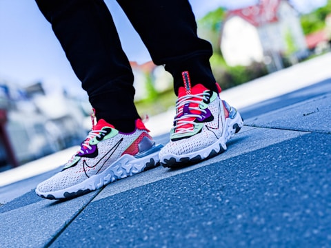 A pair of colorful athletic shoes on a person's feet, with a focus on detailed design and vibrant colors. The background is blurred with an outdoor setting giving a sense of movement or urban style.