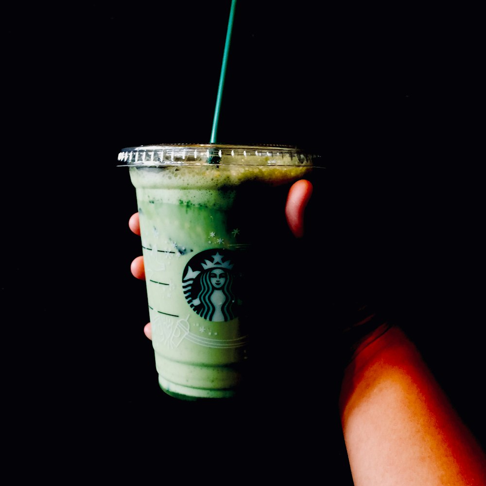 person holding white and green disposable cup with straw