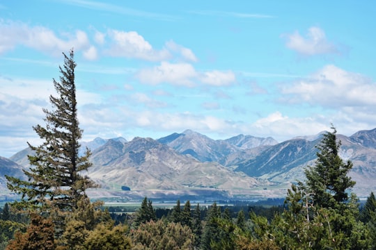 green trees near snow covered mountains under white clouds and blue sky during daytime in Hanmer Springs New Zealand