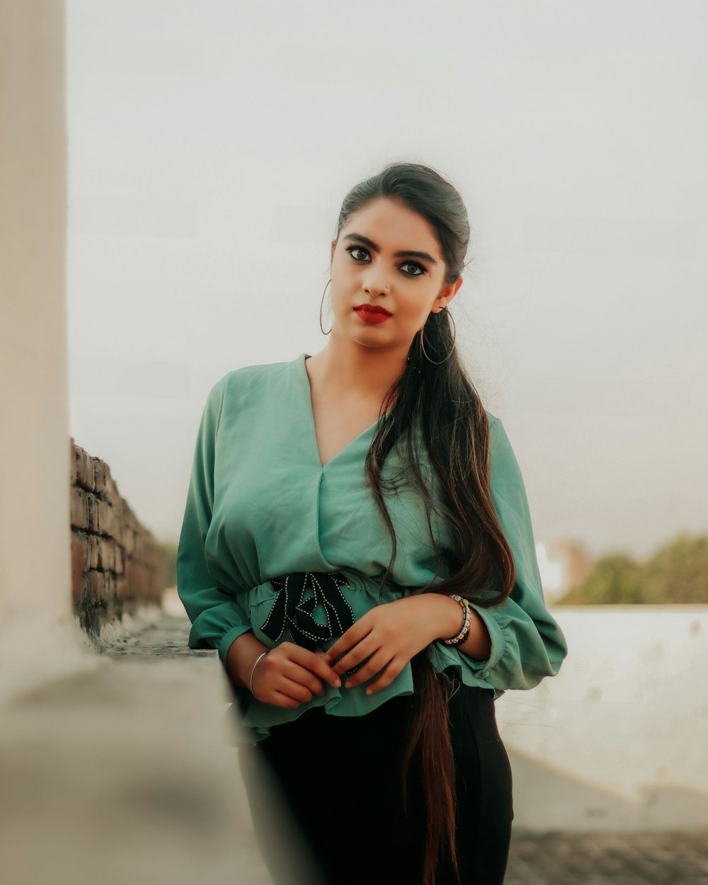 woman in green cardigan standing near white concrete wall during daytime