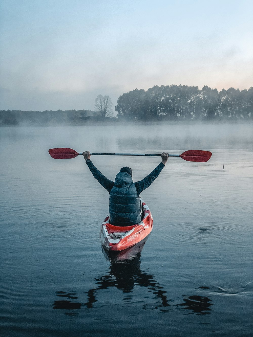 person in red and black life vest riding red kayak on body of water during daytime