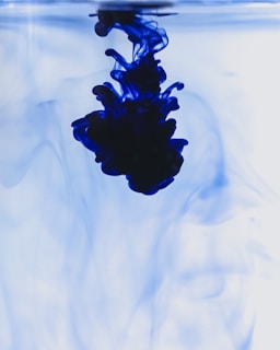 Close-up of deep blue ink swirling slowly in clear water, creating intricate, organic patterns against a dark background.