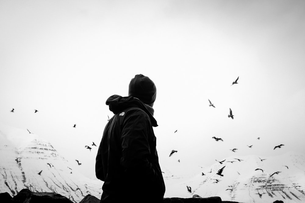 grayscale photo of man in jacket looking at birds