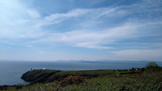 green grass field under white clouds during daytime in Baily Lighthouse Ireland