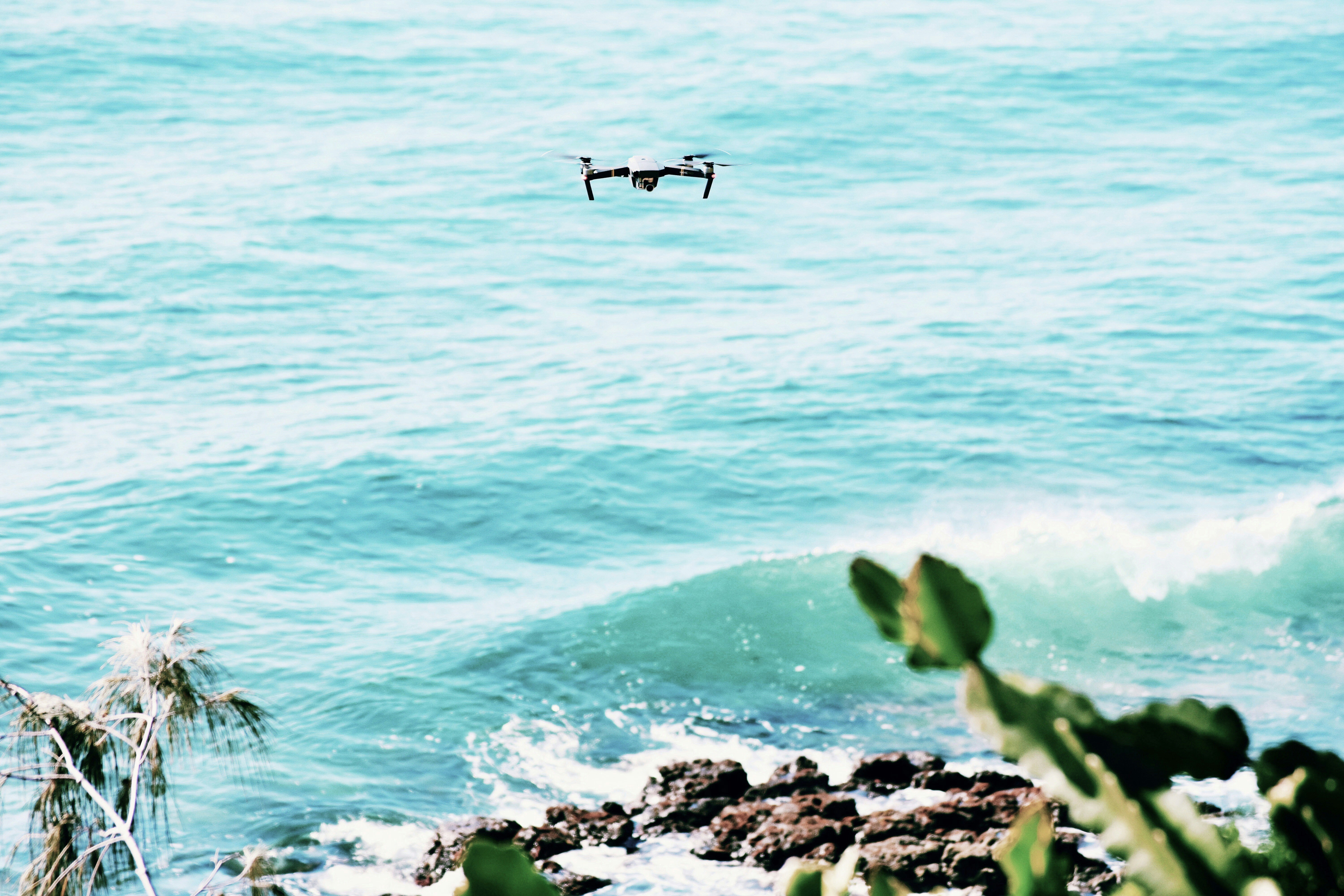 black drone flying over the sea during daytime, Drone Hovering Above the Ocean on the Sunshine Coast, Queensland, Australia.