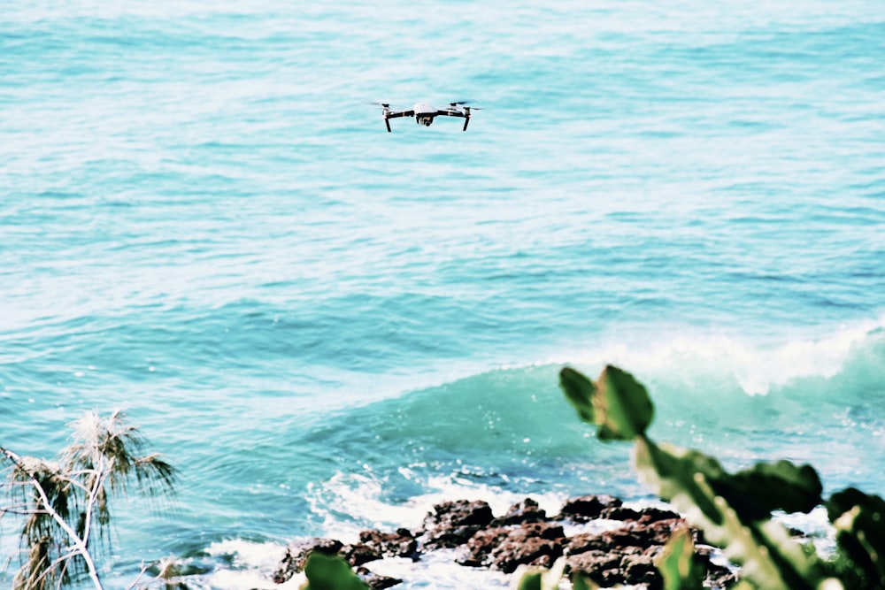 black drone flying over the sea during daytime