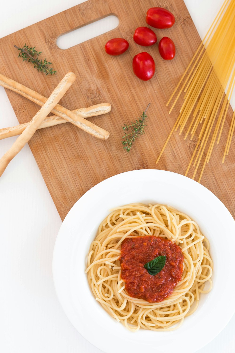 white ceramic bowl with pasta and red tomato on brown wooden table