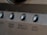 A close-up view of a brushed metal panel featuring several rounded buttons. Each button has a label, including 'ZONE 2/3/REC SELECT' and 'VIDEO SELECT'. The panel has an industrial and polished appearance with a smooth texture.