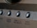 A close-up view of a brushed metal panel featuring several rounded buttons. Each button has a label, including 'ZONE 2/3/REC SELECT' and 'VIDEO SELECT'. The panel has an industrial and polished appearance with a smooth texture.