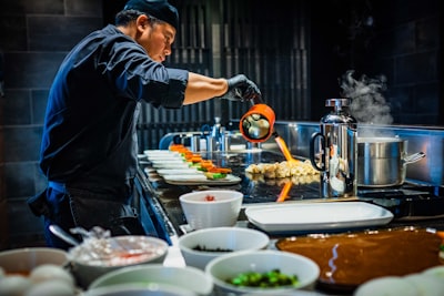 man in blue jacket pouring water on white ceramic bowl cook teams background