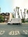 A white delivery van with graffiti covering its side is parked on a street lined with residential buildings and pruned trees. The pavement has clear road markings saying 'KEEP CLEAR'. The sky is clear and blue, with some buildings and green foliage visible in the background.