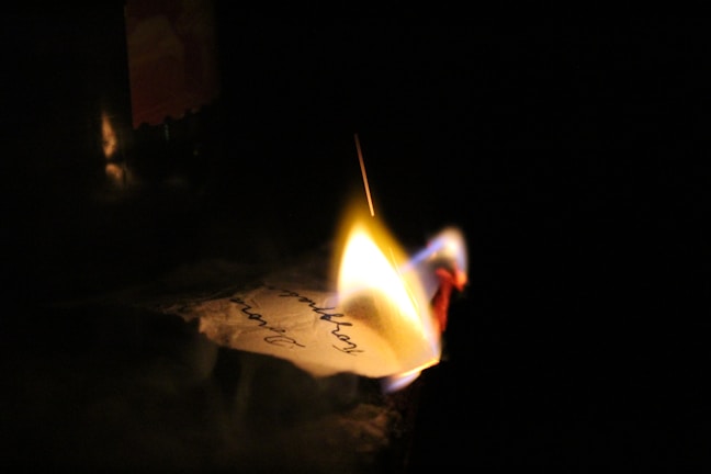 A handwritten note with reflections beside a flickering candle.