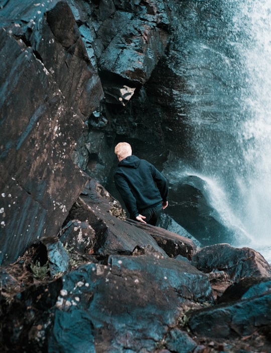 man in black jacket sitting on rock near water falls during daytime in Saint-Côme Canada