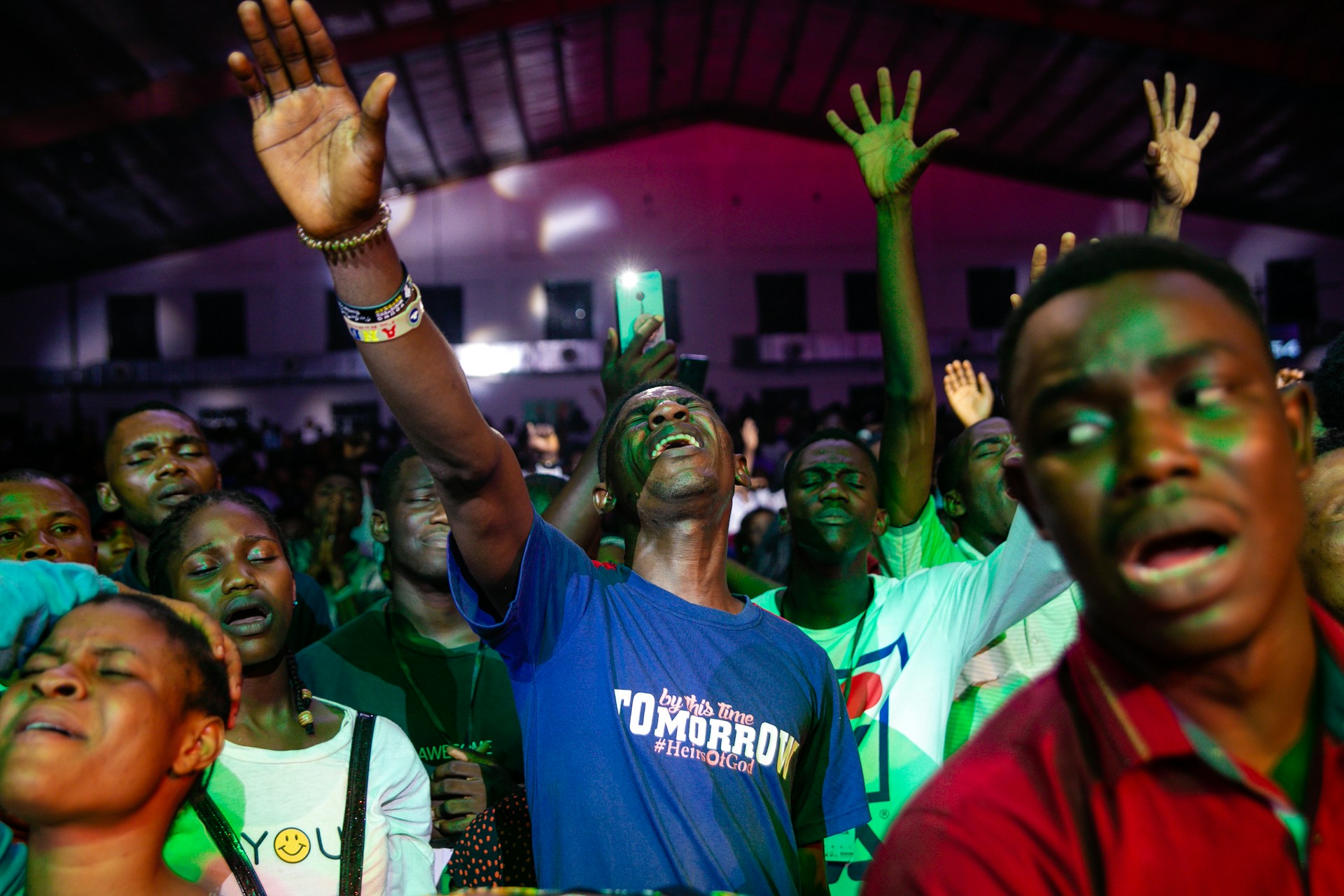 A crowd united in worship, faces lifted and eyes closed, bathed in flickering fire orange hues blending into black shadows.