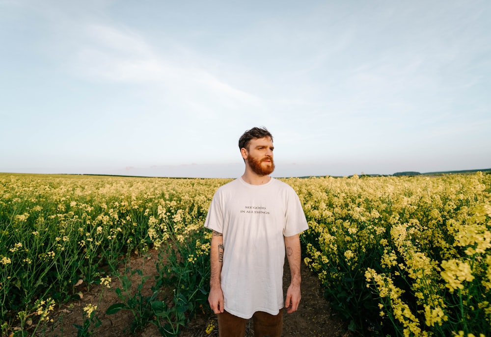 man in white crew neck t-shirt standing on yellow flower field during daytime