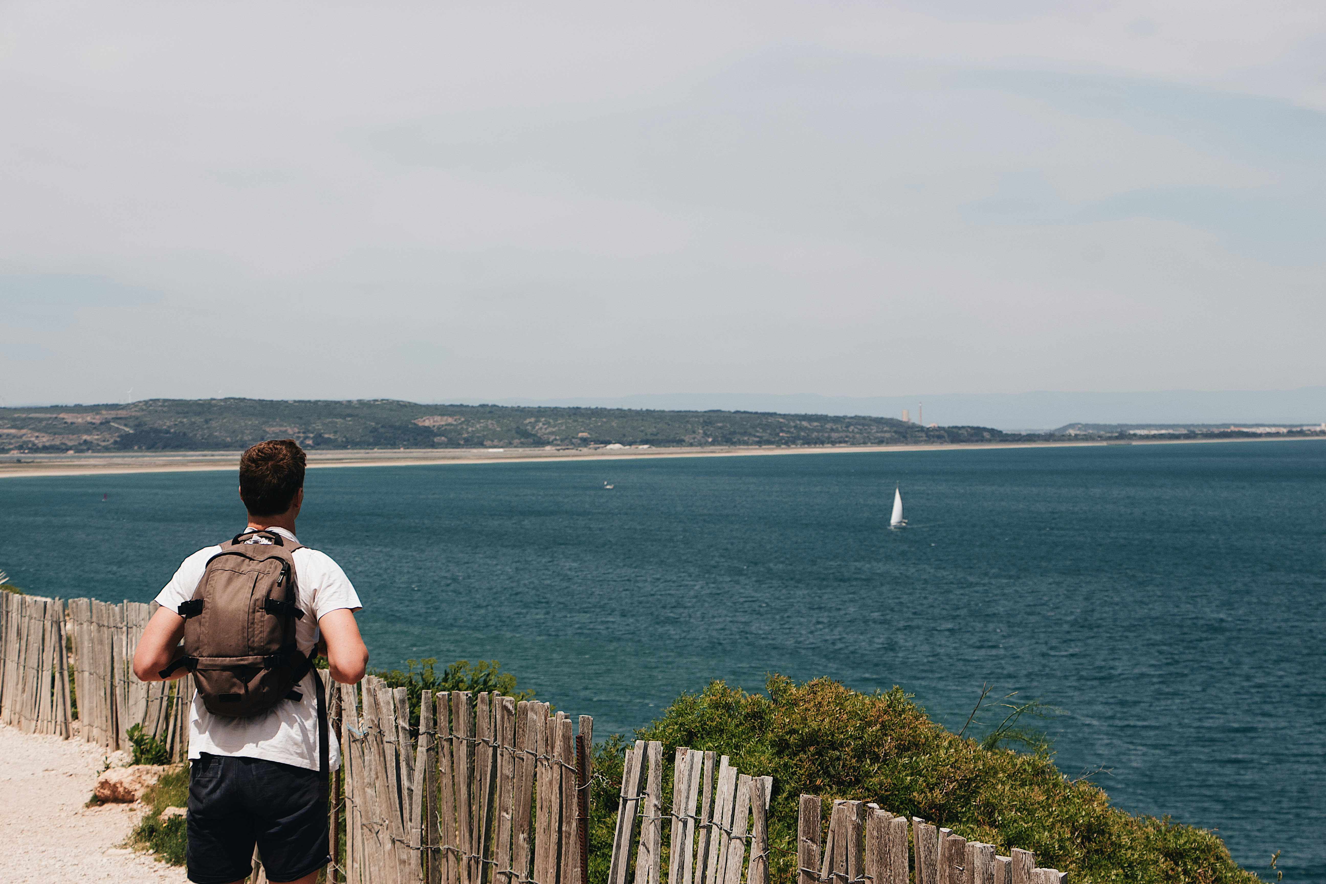 woman in white shirt standing on wooden fence looking at sea during daytime