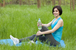 woman in blue tank top and black pants sitting on green grass field