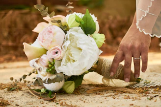 A bride's hand gently holding a vibrant bouquet of mixed roses in white, baby pink, and warm hues, radiating a soft, romantic glow.