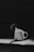 A ceramic mug with a speckled pattern and the text 'Wonder Wo-Mum' sits on a surface. Steam rises from the mug, indicating hot liquid inside. The scene is dimly lit, with a strong contrast between light and shadow.