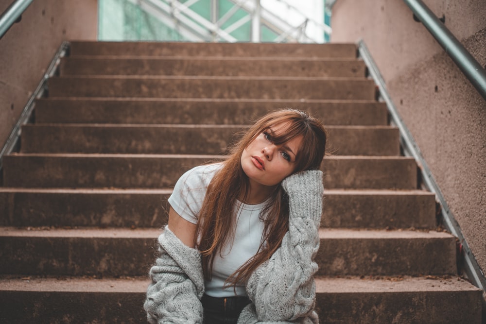 Femme en cardigan gris assise sur des escaliers en béton brun