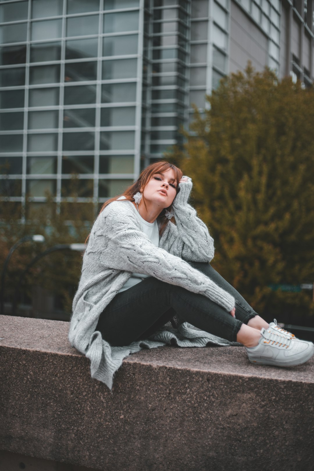 woman in gray coat sitting on brown concrete bench during daytime