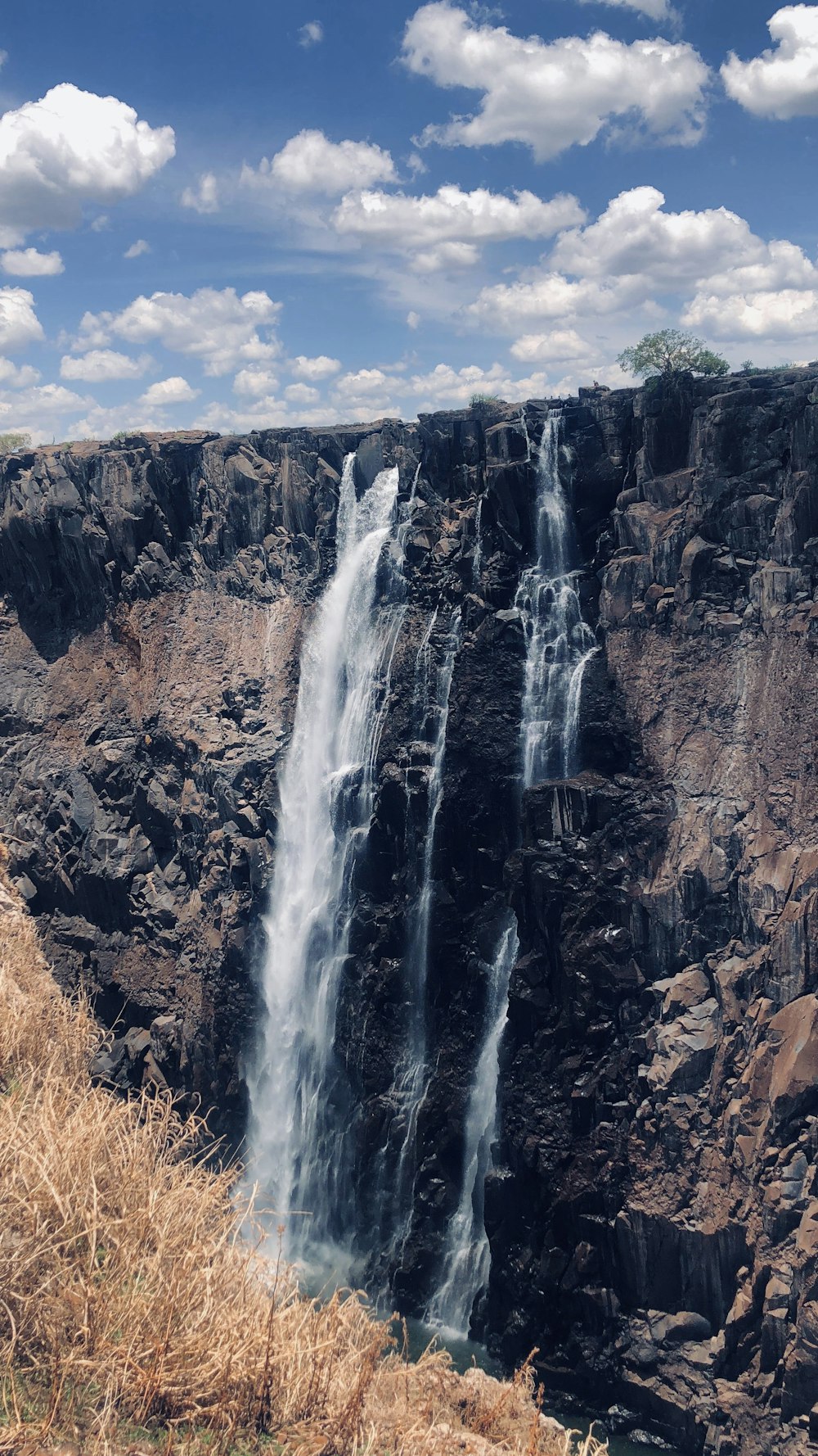 waterfalls on brown rocky mountain under blue sky during daytime