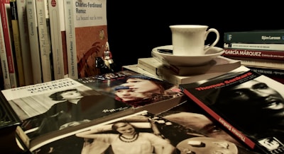 A neat stack of popular novels and non-fiction books with a cup of coffee nearby.