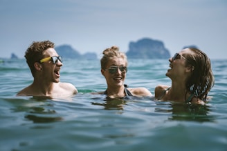 Three friends laughing together around a microphone with a desert island backdrop.