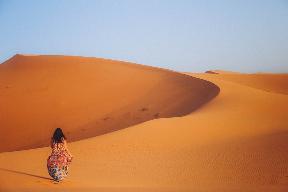 woman in blue and white floral dress sitting on brown sand