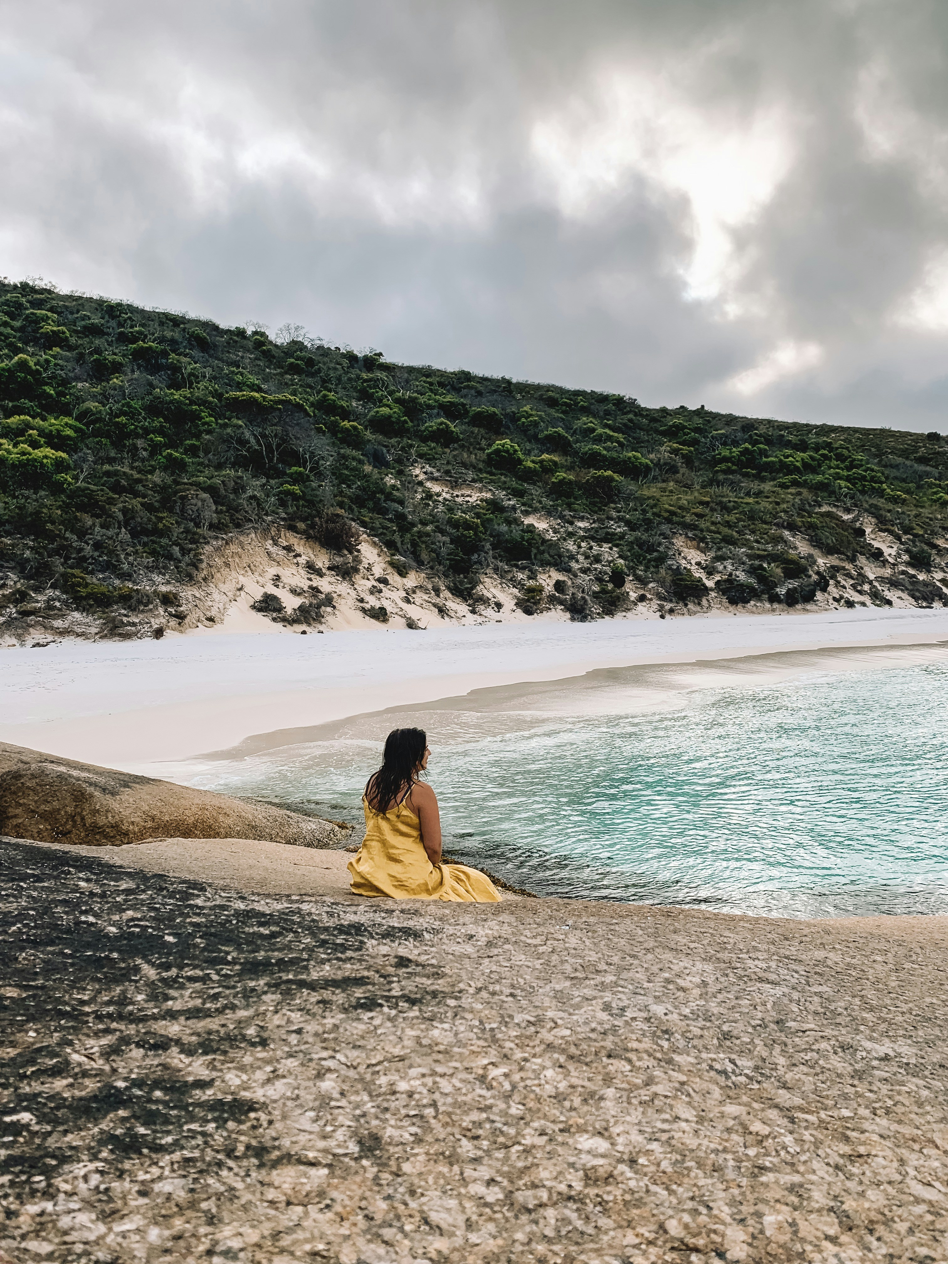 woman in yellow dress sitting on brown rock near body of water during daytime
