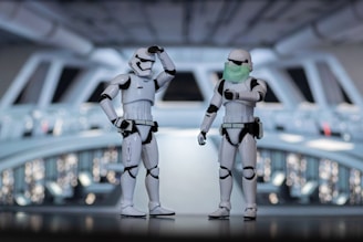 Two stormtrooper figures are standing in a detailed sci-fi setting that appears to resemble a spaceship or space station. One stormtrooper is saluting while the other is pointing and wearing a green face mask.