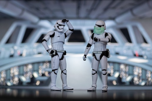 Two stormtrooper figures are standing in a detailed sci-fi setting that appears to resemble a spaceship or space station. One stormtrooper is saluting while the other is pointing and wearing a green face mask.