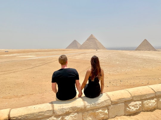 man and woman sitting on concrete wall during daytime in Giza Necropolis Egypt