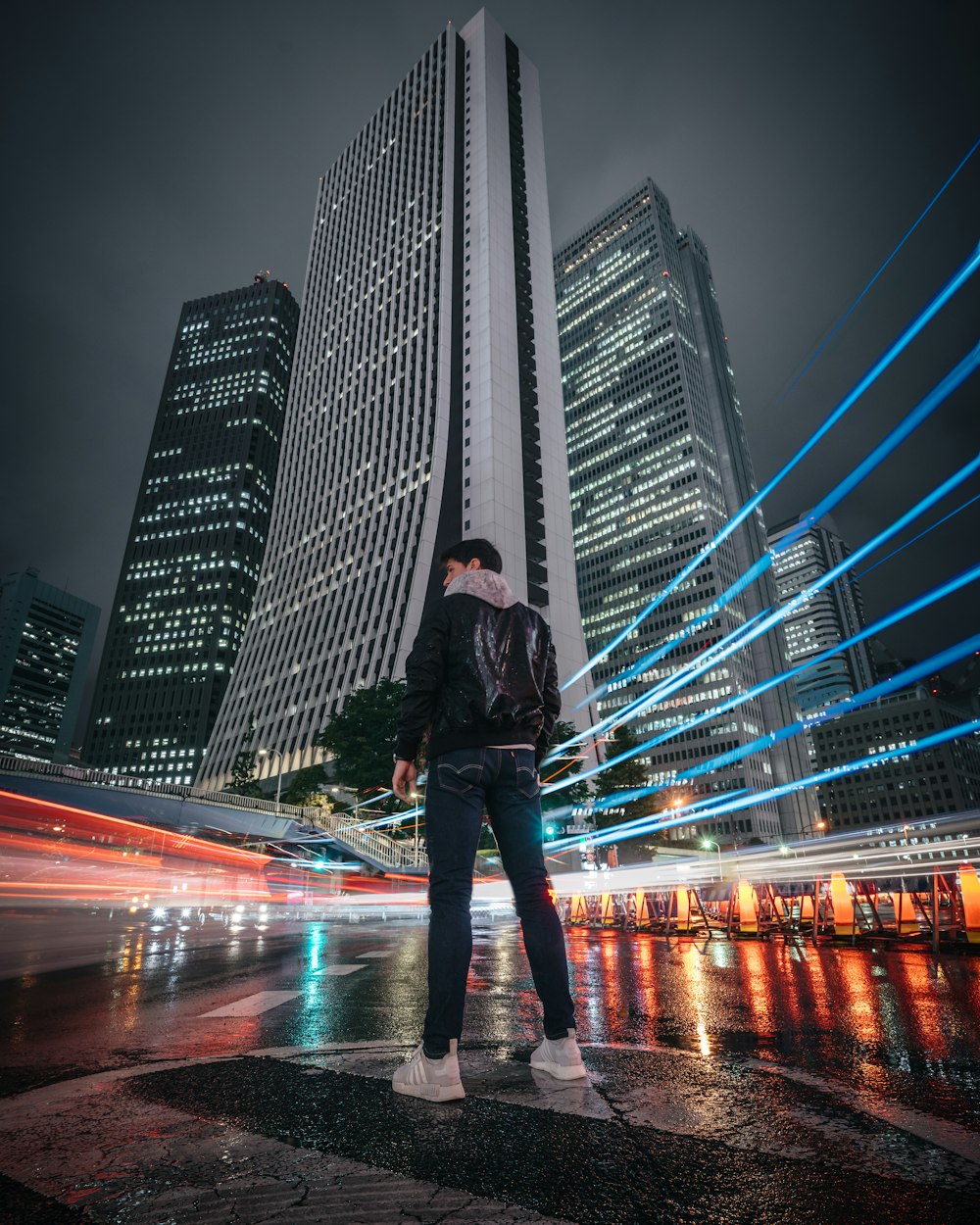 man in black jacket and blue denim jeans standing on road during night time