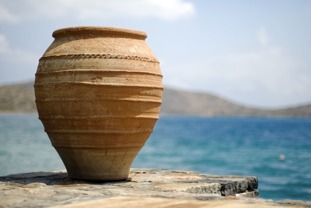 vaso de barro marrom na areia branca perto do corpo de água durante o dia