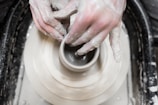 A child shaping a small clay bowl on a pottery wheel, hands covered in wet clay.
