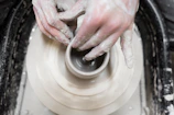 Hands shaping a clay pot on a spinning wheel, dusted with soft clay powder.