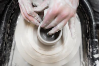 A pair of hands gently shaping a clay pot on a spinning wheel, with splashes of colorful glaze nearby.