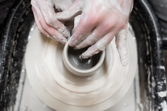 Close-up of a craftsman shaping a clay pot with hands covered in wet clay.